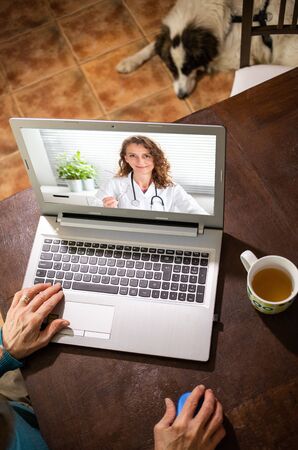 telemedicine concept elderly woman in an online consultation on video call from her kitchen taking her blood pressureの写真素材