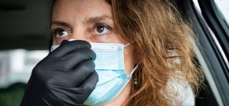 woman putting on medical mask in her car safety measures during pandemicの写真素材