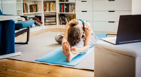 woman doing yoga asanas at home with laptopの写真素材