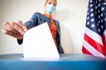 woman wearing mask putting vote in ballot