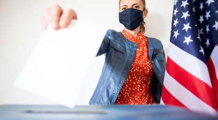 woman wearing mask putting vote in ballotの写真素材
