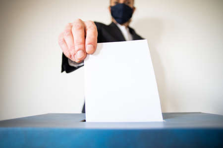 woman wearing mask putting vote in ballot