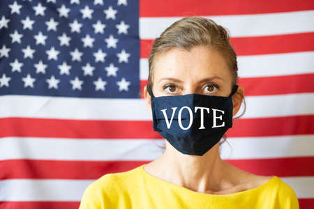 woman wearing mask in front of USA flag elections during covidの写真素材