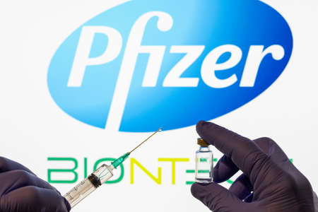 CLUJ-NAPOCA -ROMANIA - MARCH 9 2021: Pfizer vaccine Covid-19 concept. Syringe needle and vaccine, blurred Pfizer company logo on the background.のeditorial素材