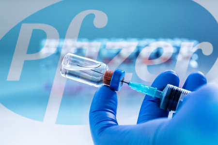 CLUJ-NAPOCA -ROMANIA - MARCH 9 2021: Pfizer vaccine Covid-19 concept. Syringe needle and vaccine, blurred Pfizer company logo on the background.のeditorial素材