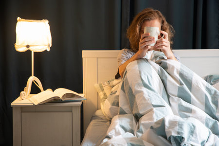 woman with coffee or tea cup in bed night time restの写真素材