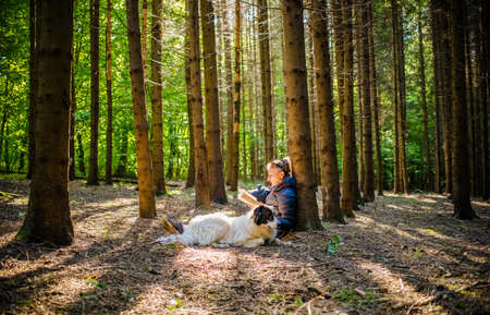 woman with dog reading a book in forestの写真素材