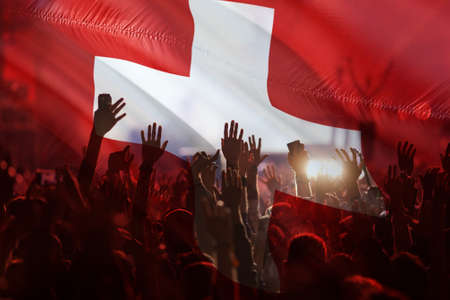 football fans supporting Switzerland - crowd celebrating in stadium with raised hands against Switzerland flagの写真素材