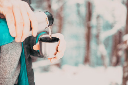 man pouring hot tea in winter forestの写真素材