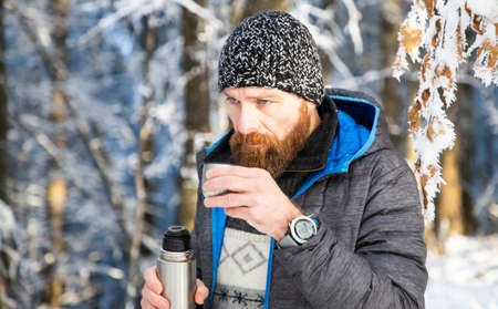 man drinking hot tea in winter forest