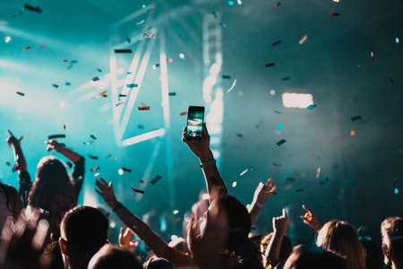 cheering crowd with raised hands and falling confetti at concert - music festivalの写真素材