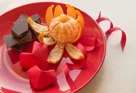 Two volumetric hearts of paper. Red plate with chocolate and mandarin in the shape of a flower.  Valentine's Day. March 8. International Women's Day.の写真素材