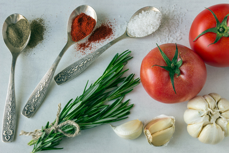 Herbs and spices in metal spoons on a light background. Ingredients for cooking. Tomatoes and garlic.の写真素材