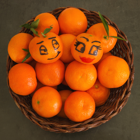 Bright juicy tangerines with leaves in a wicker basket. Funny faces drawn on two tangerines .の写真素材