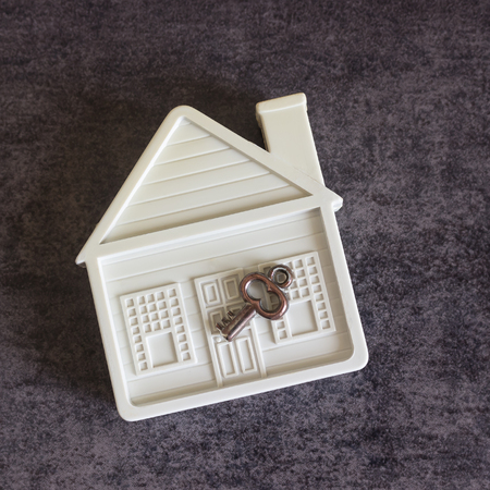 Small white house and a decorative key on a dark background. Concept  -  real estate purchase, sale, gift, rent.の写真素材