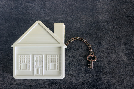 Small white house and a decorative key on a dark background. Concept  -  real estate purchase, sale, gift, rent.の写真素材