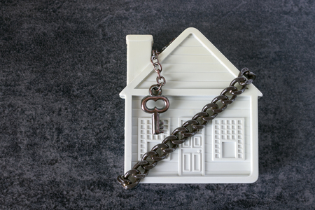 Small white house, chain and a decorative key on a dark background. Concept  -  risks, lose property,  seize, mortgage.の写真素材