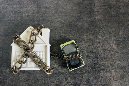 Small white house, car and a decorative chain on a dark background. Concept  -  risks, lose property,  seize, mortgage.の写真素材