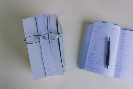 A stack of thick new books and black glasses  depict a person's face. Concept- reading, preparation for exams, training. Selective focus.の写真素材
