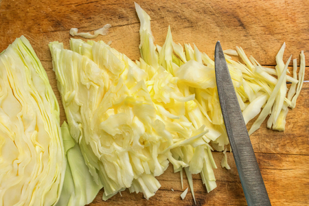 White cabbage is sliced for salad. Located on a wooden board next to the knife. Concept- vegetarianism, raw food, recipe.の写真素材