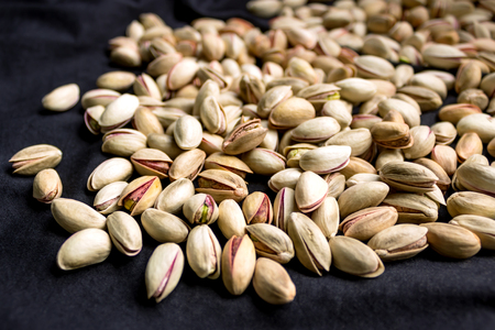 Pistachios are scattered on the black fabric. A full source of vegetable protein in vegetarianism and raw food. Concept - healthy eating. Selective focus.の写真素材
