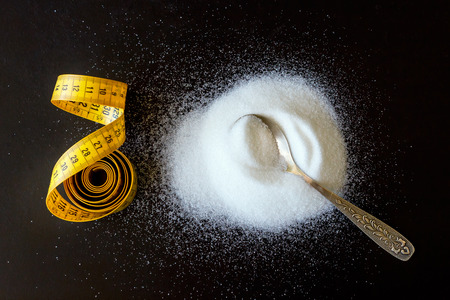 Coiled yellow tape measure and a spoon filled with sugar. The concept is healthy eating, diet, control and weight loss.の写真素材