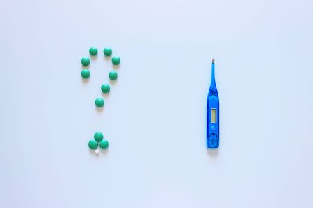 Blue thermometer on a light background. Question mark is made up of colored tablets. The concept of choice of treatment.の写真素材