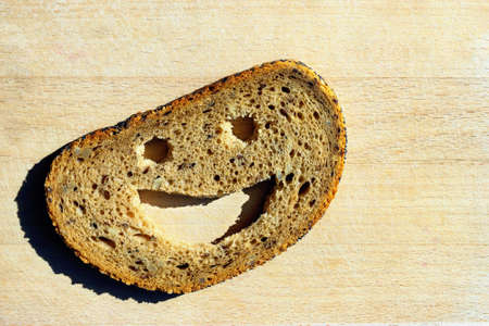 Slice of rye bread with a smiling face. Texture of fresh homemade bread with seeds. Concept -...