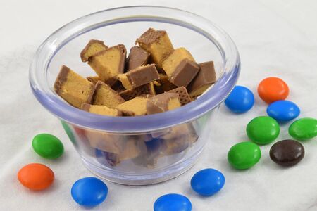 Colorful milk chocolate candies scattered around a glass bowl full of delicious chocolate and peanut butter candy.の写真素材