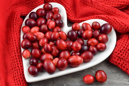 Fresh red cranberries on a heart shaped plate encircled by a textured red kitchen towel. Concept for heart health month and Valentine's Day.の写真素材