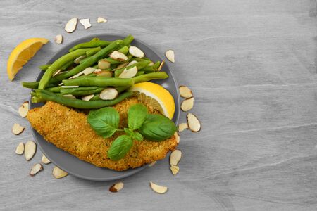 Golden brown parmesan encrusted tilapia topped with a sprig of fresh basil. Buttered green beans, sliced almonds and lemons grace the plate of this gourmet meal. Plenty of copy space.の写真素材