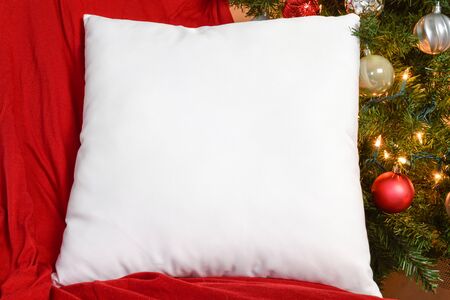 White Square PIllow Mockup Resting on Red Blanket with Lit Up Christmas Tree in Backgroundの写真素材