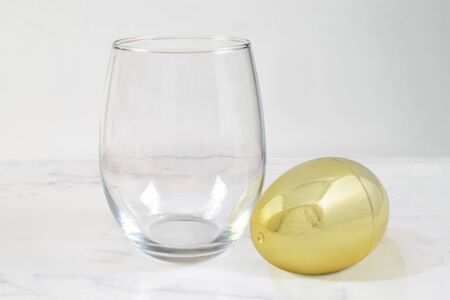 A classy no stem wine glass rests luxuriously next to a golden Easter egg.の写真素材