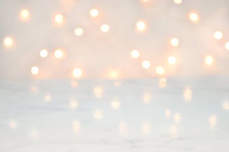 A strand of white Christmas lights defocused in the background to create a glowing bokeh pattern. The glossy white marble surface reflects the pretty white lights.の写真素材