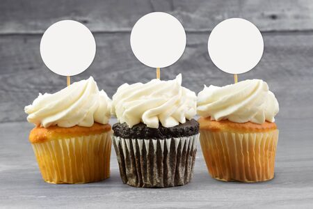 Cupcake topper mockup featuring chocolate and yellow cupcakes sitting temptingly on a gray wooden background.の写真素材