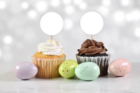 Gourmet chocolate and vanilla cupcakes surrounded by colorful speckled Easter eggs. Bokeh lights add a touch of flair to this Easter cupcake topper mock up.の写真素材