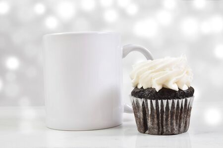 A white 11 ounce coffee cup chills gracefully next to a tempting chocolate cupcake with white frosting. A white light effect glows luxuriously in the background.の写真素材
