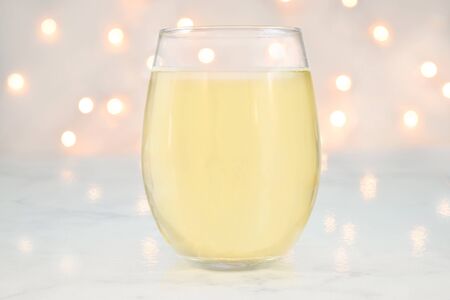 No Stem Wineglass mockup featuring a stemless wine glass filled with white wine. White lights glow romantically in the background.の写真素材