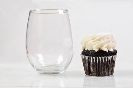 No stem wine glass resting happily next to a tempting chocolate cupcake.の写真素材