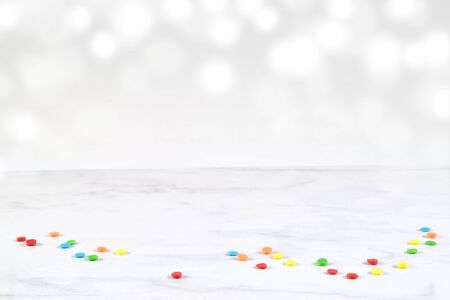 Colorful sprinkles scattered on white marble background with bokeh light effect shining in the background.の写真素材