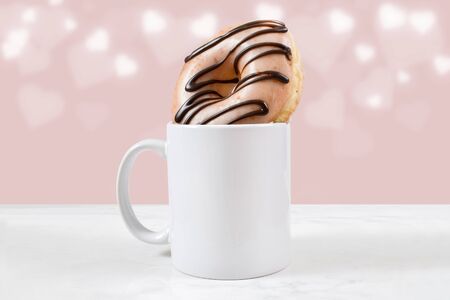 White coffee mug filled with a glazed chocolate ice donut.の写真素材