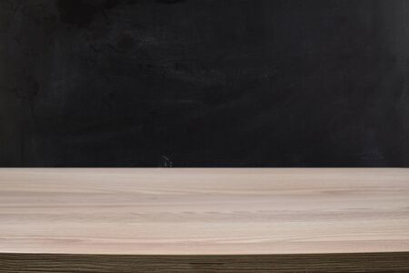 Light wood table against a black chalkboard wall.の写真素材
