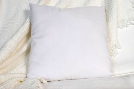 A square white throw pillow rests lazily against a pretty white blanket.の写真素材