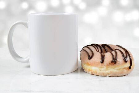 An 11 ounce white coffee cup sits next to a glorious glazed and chocolate iced donut.の写真素材