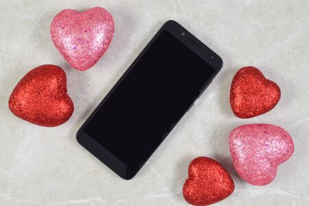 A smart phone chills romantically atop a stone background surrounded by glittery hearts.の写真素材