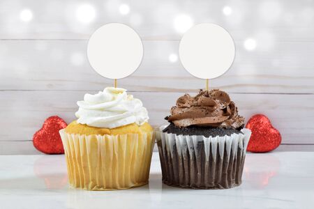 A gourmet chocolate and vanilla cupcake rest between two glittery red hearts in this Valentine cupcake topper mockup.の写真素材