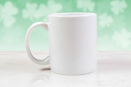 An 11 ounce white coffee cup chills atop a white marble background. Shamrocks glow in the background.の写真素材