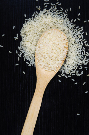 Golden uncooked rice on wooden spoon on dark tableの写真素材