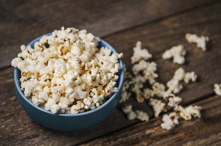 Popcorn in a blue bowl on wooden tableの写真素材