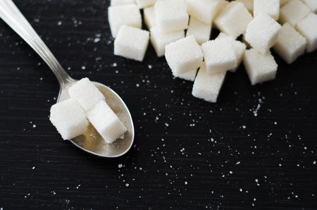 White sugar cubes piled in a heap on the black desk with spoonの写真素材